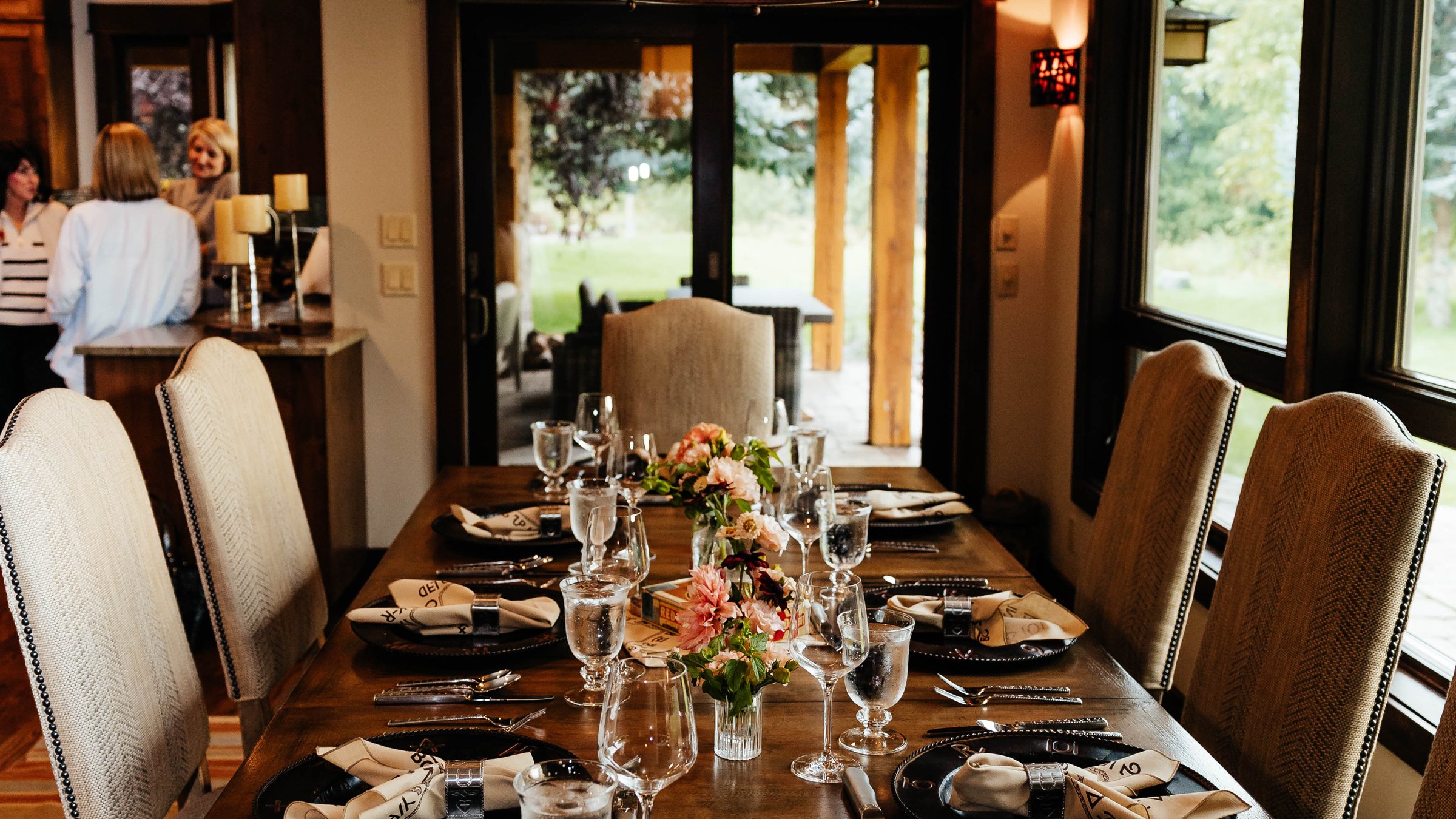 Long table set for a private dinner with flowers, glassware, and a hanging lantern
