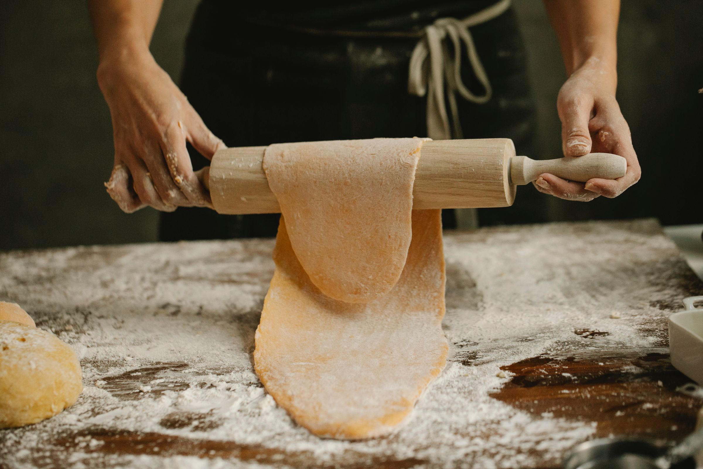 Hands rolling out fresh pasta dough on a floured table
